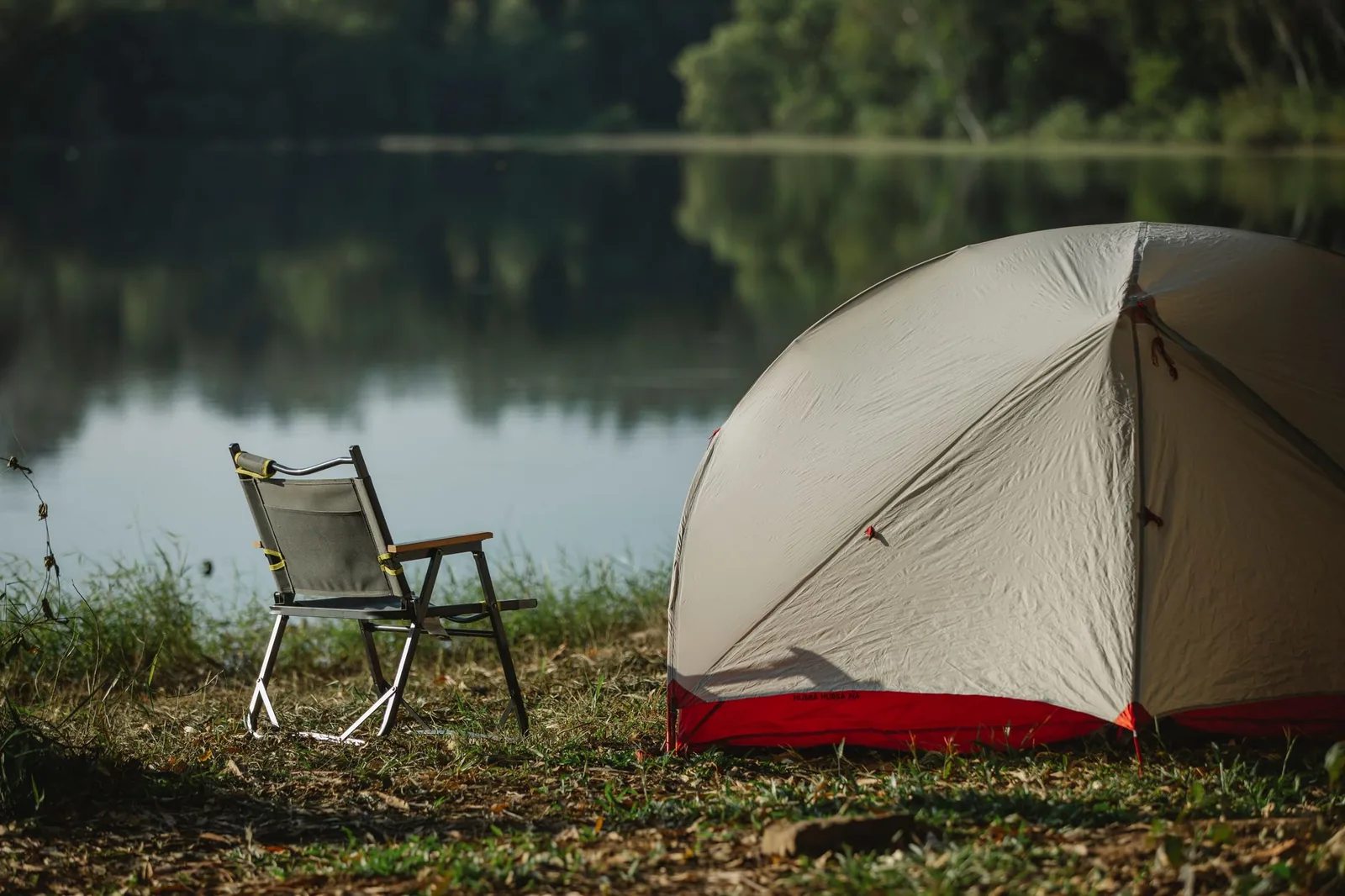 Grauer Klappstuhl mit gepolsterten Armlehnen auf einer Wiese im Campingumfeld