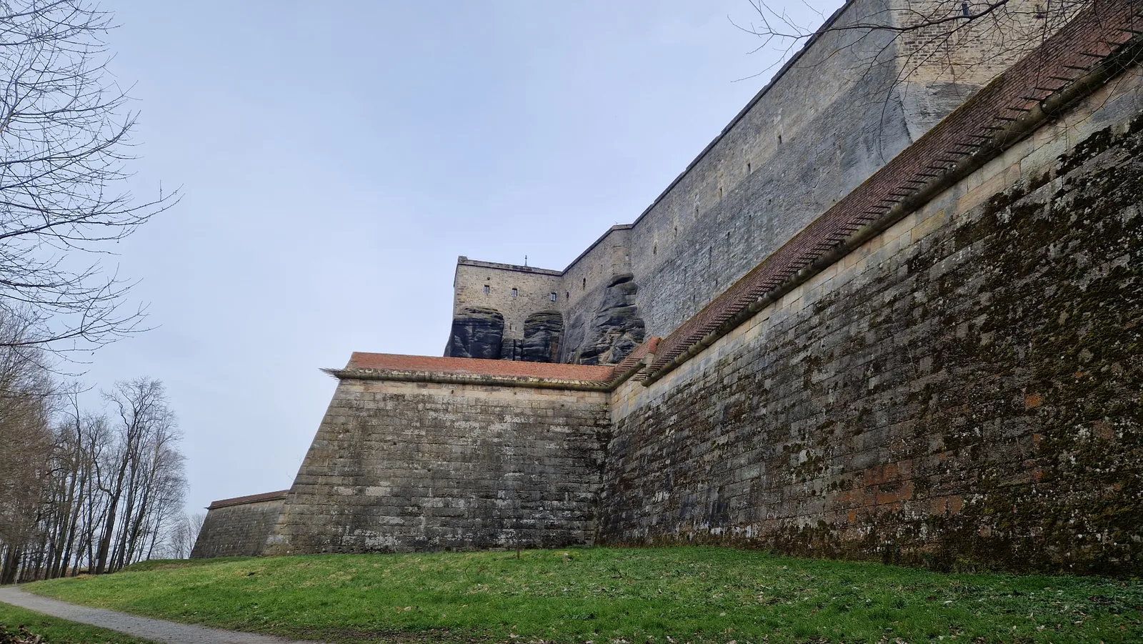 Massive Festungsmauer der Festung Königstein von außen, mit Wiese im Vordergrund